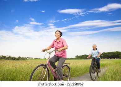 Happy Asian Elderly Seniors Couple Biking In Farm With Blue Sky Background