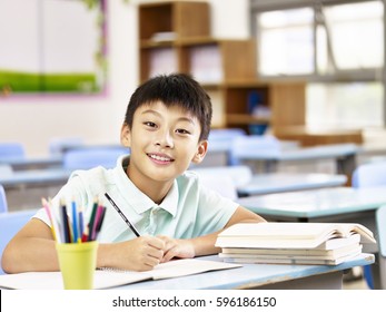 happy asian elementary school boy studying in classroom, looking at camera smiling.