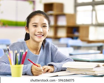 happy asian elementary school student studying in classroom looking at camera smiling,
