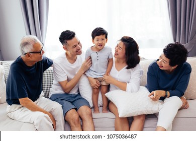 Happy Asian Extended Family Sitting On Sofa Together, Posing For Group Photos