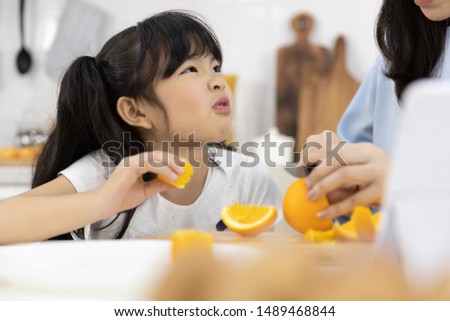 Happy Asian family Close up of Little girl eating Orange fruit and Mother are preparing the vegetables and fruit in the kitchen at home. Healthy food concept