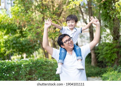 Happy Asian Family Concept, Little Happy Young Boy Playing With His Father At The Garden, A Boy Climbing On His Father Back. Asian Dad And Son Portrait.