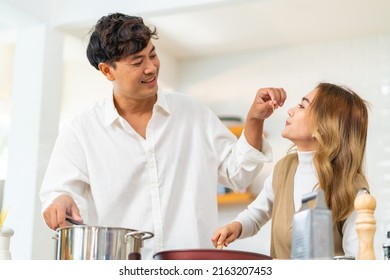 Happy Asian Family Couple Enjoy Cooking Pasta On Cooking Pan With Talking Together In The Kitchen At Home. Husband And Wife Having Dinner Party Celebration Eating Food Together On Holiday Vacation