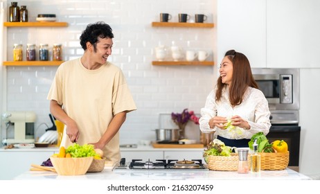 Happy Asian Family Couple Enjoy Cooking Pasta On Cooking Pan With Talking Together In The Kitchen At Home. Husband And Wife Having Dinner Party Celebration Eating Food Together On Holiday Vacation