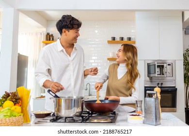 Happy Asian family couple enjoy cooking pasta on cooking pan with talking together in the kitchen at home. Husband and wife having dinner party celebration eating food together on holiday vacation