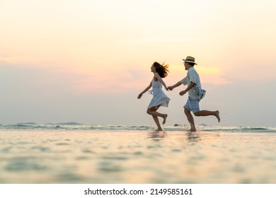 Happy Asian family couple holding hand and walking together on tropical beach at summer sunset on beach vacation. Cheerful husband and wife relax and enjoy outdoor lifestyle on holiday travel vacation - Powered by Shutterstock