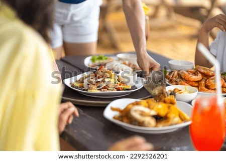 Happy Asian family couple and little kids travel ocean on summer holiday vacation. Waitress serving food and drink to customers on the table at beach restaurant at tropical island beach in sunny day.