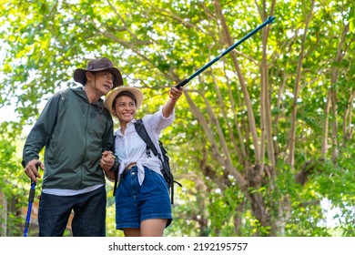 Happy Asian Family Couple On Summer Holiday Vacation. Mature Adult Couple Hiking Together In Forest. Man And Woman Enjoy Outdoor Lifestyle Trekking And Looking To Green Wood On Summer Travel Vacation.