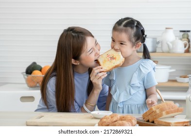 Happy Asian family, cute little daughter and young mother enjoy eating bread with jam and rainbow sugar flakes after spreading jam on sliced bread together, preparing breakfast in kitchen at home - Shutterstock ID 2172869321