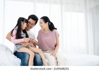 Happy asian family with daughter playing together at home. Parents are having fun on the bed