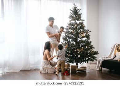 Happy Asian family decorating Christmas tree together in the living room at home. They are putting on various baubles and ornaments and enjoying their holiday - Powered by Shutterstock