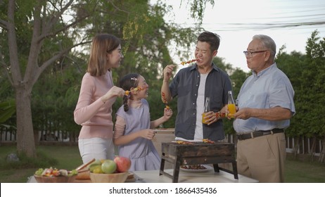 Happy Asian Family Dining And Tasting Juice On Glasses In Barbecue Dinner Party, Multi Generation Family Enjoying Meal Together. People Having Outdoor Party Eating Food At Backyard Home In Garden.