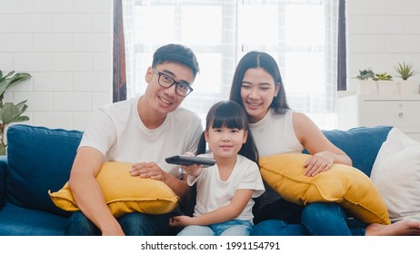 Happy Asian Family Enjoy Their Free Time Relax Together At Home. Lifestyle Korean Dad, Mom And Daughter Watching TV Together And Having Fun Lying On Sofa In Living Room In Modern House.