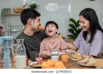 Happy Asian Family Enjoying Breakfast Together On Dinning Table. Young Asian Father Eating Bread With Family His Son And Wife Having Breakfast In The Kitchen. Happy Asian Family Lifestyle Concept.