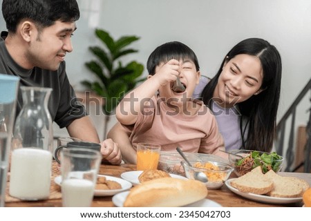 Happy Asian family enjoying breakfast together on dinning table. Young Asian mother feeding vegetable to her son while having breakfast in the kitchen. Healthy food family activity lifestyle concept. Imagine de stoc © 