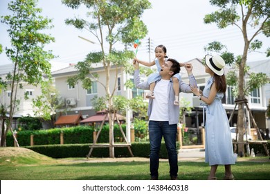 Happy Asian Family. Father Gave His Daughter A Piggyback At A Park At Natural Sunlight Background And House. Family Vacation Concept With Copy Space