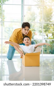 Happy Asian Family, Father Having Fun With Son While Pushing Carton Box In Living Room.Young Family Enjoy Moving To New Home On Relocation Day.