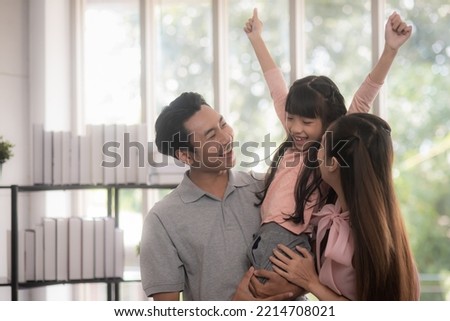 Happy asian family, A father holds his daughter and mother stands close to the two of them, laughing happily in the living room. spending time together forming and closer a family bond.