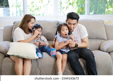 Happy Asian Family, Father, Mother Daughter And Son Singing Karaoke On The Sofa In The Living Room With Happy Smiling Face (relaxation And Technology Concept)