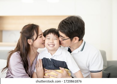 Happy Asian Family, Father And Mother Kissing Boy Smile Together In Living Room And Kitchen Room In Background, Parent And Kid Is Real People Family.