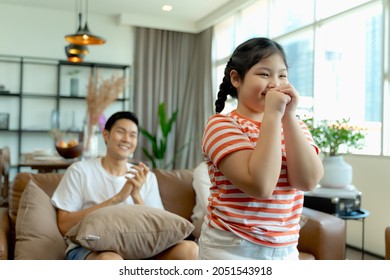 Happy Asian Family, Father, Mother And Daughter Singing Karaoke On The Sofa In The Living Room At Home With Happy Smiling Face 