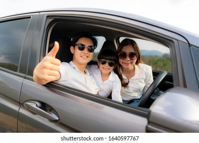 Happy Asian Family With Father Thumb Up And Mother And Daughter Wear Sunglass In Compact Car Are Smiling And Driving For Travel On Vacation. Car Insurance Or Rental 
