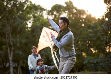 happy asian family flying a kite outdoors in city park - Powered by Shutterstock