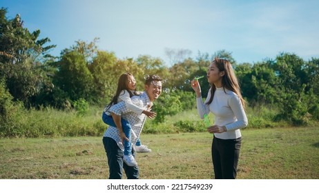 Happy Asian Family In The Garden They Are Having Fun Playing And Blowing Bubbles. And Enjoyed Ourselves Together In The Green Garden. Family Enjoying Sunny Fall Day In Nature.