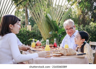 Happy Asian Family Having To Enjoy A Meal(pizza, Salad, Snack, Orange Juice) Together At Home Garden