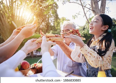 Happy Asian Family Having Enjoying Meal(pizaa, Salad,snack, Orange Juice) Together In Home Garden. Outdoor Dinner Party In Holiday. Multi Generation Family Concept.