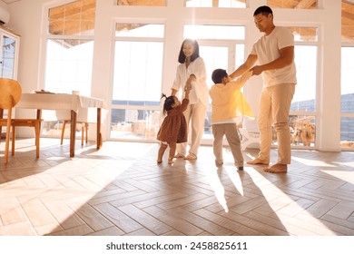 Happy Asian family is having fun at home. Korean young parents dancing with cute little kids in dining room. Mom and dad and their children are move their body to song in cozy interior with daylight. - Powered by Shutterstock