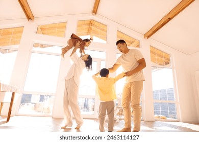 Happy Asian family is having fun at home. Korean young parents dancing with cute little kids in dining room. Mom and dad and their children are move their body to song in cozy interior with daylight. - Powered by Shutterstock