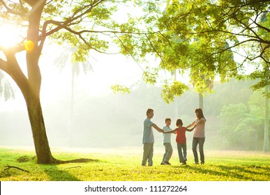 Happy Asian family holding hands in a circle and running over green lawn