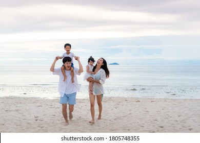 Happy Asian Family Holidays During Joyful Father, Mother, Son And Daughter Walking Together Along Summer Sunset Sea. Happy Family Travel On Beach In Holiday, Summer And Vacation.