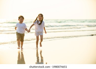 Happy Asian Family Little Brother And Sister Running And Playing Together On Beach At Summer Sunset. Two Child Kid Girl And Boy Sibling Enjoy And Having Fun Outdoor Activity In Summer Travel Vacation