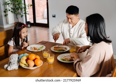 Happy Asian Family With Little Daughter Having Breakfast Over Table At Home