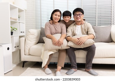Happy Asian family with little son sitting on sofa together in living room at home
