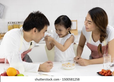 Happy Asian Family Make A Cooking. Father, Mother And Daughter Are Eating Breakfast, Cereal With Milk In The Kitchen At Home. Healthy Food Concept And Happy Holidays