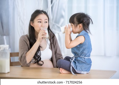 Happy Asian Family Mom And Daughter Drink Milk At Home .