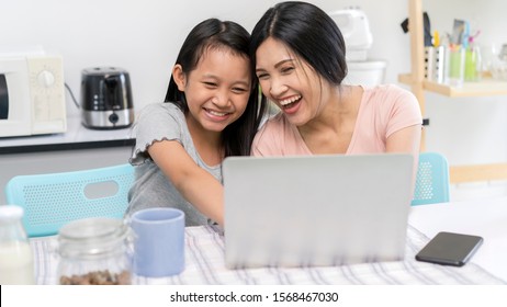 Happy Asian Family. Mother And Daughter Together Using A Laptop Or Livestream Or Watch Media Online Laugh While Spending Time. Cheerful Parent And Kid With Laptop For Watching English Practice Cartoon