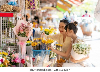 Happy Asian family mother and daughter choosing and buying fresh flower together at florist shop street market for flower vase arrangement celebrating holiday event on summer vacation at home