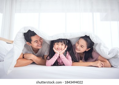 Happy Asian Family (mother, Father, Child Daughter) Laying On Bed While Smile In Bedroom At Home.