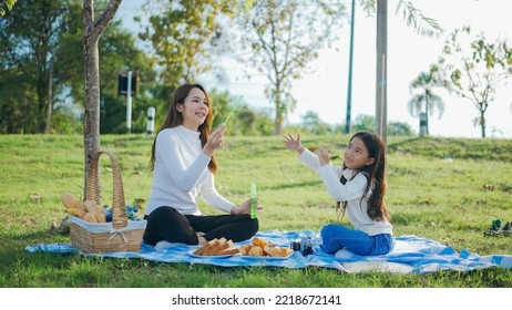 Happy Asian Family Mother And Her Daughter In The Garden, They Are Having Fun Playing And Blowing Bubbles. Family Enjoying Sunny Fall Day In Nature.