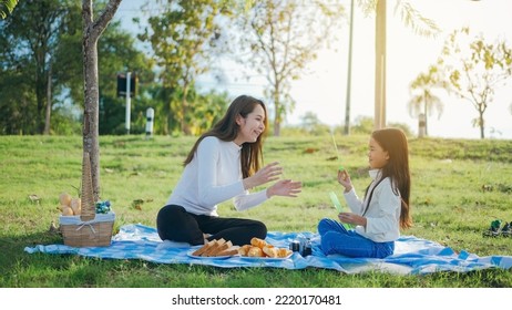 Happy Asian Family Mother And Her Daughter In The Garden, They Are Having Fun Playing And Blowing Bubbles. Family Enjoying Sunny Fall Day In Nature.