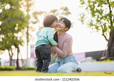 Happy asian family mother and  kid spending time together at the park. Kissing each other. Have fun enjoy family time at weekend  with beautiful sun light. Lifestyle Childhood and weekend concept