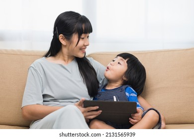 Happy Asian Family Mother And  Son Using Tablet For Education. Little Boy Watching Funny Social Media.  Mom With Kid Using Tablet Video Call To Father.