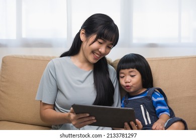 Happy Asian Family Mother And  Son Using Tablet For Education. Little Boy Watching Funny Social Media.  Mom With Kid Using Tablet Video Call To Father.
