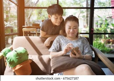 Happy Asian Family. Mother And Son Looking At Screen Of Cell Phone With Sun Light In The Morning At Home