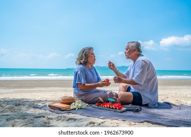 Happy Asian Family On Beach Vacation. Senior Couple Sitting On Blanket Have Picnic Together On Sea Beach. Healthy Elderly Husband And Wife Relax And Enjoy Outdoor Lifestyle Activity On Summer Vacation