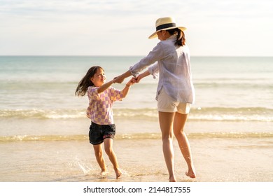 Happy Asian family on beach vacation. Mother and little daughter walking and playing together on tropical beach at summer sunset. Mom and child girl kid enjoy and fun outdoor lifestyle on the beach